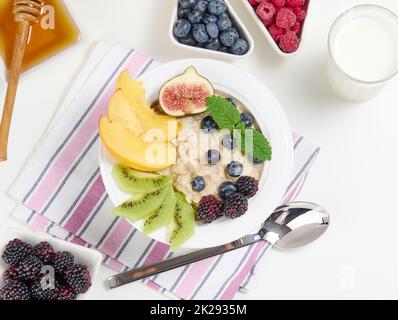 latte, piatto con porridge di farina d'avena e frutta, miele in una ciotola su un tavolo bianco. Colazione sana Foto Stock