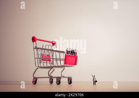 Persone in miniatura sedute su un gigantesco carrello della spesa. Concetto di risparmio e shopping Foto Stock