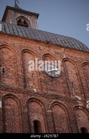 Un orologio a torre è blasonato su un grande edificio di mattoni chiesa. Foto Stock