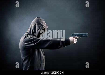 Uomo incappucciato con una pistola nel buio Foto Stock