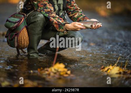 Vista ravvicinata delle mani di un pescatore a mosca in possesso di una bella trota mentre la pesca con la mosca su di uno splendido fiume di montagna Foto Stock