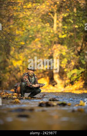 Vista ravvicinata delle mani di un pescatore a mosca in possesso di una bella trota mentre la pesca con la mosca su di uno splendido fiume di montagna Foto Stock