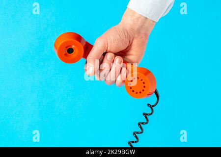 Tenere il vecchio ricevitore telefonico su sfondo blu Foto Stock