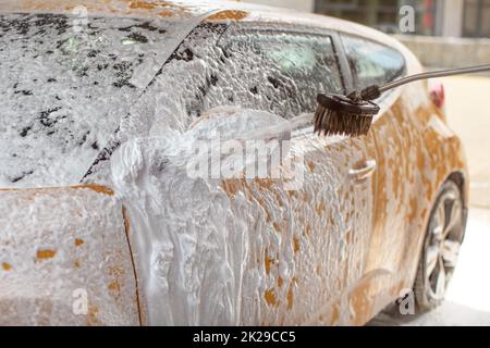 Giallo auto lavata in self service autolavaggi. Shampoo la spruzzatura a specchio laterale, già coperti in schiuma bianca, scende la spruzzatura ovunque. Foto Stock