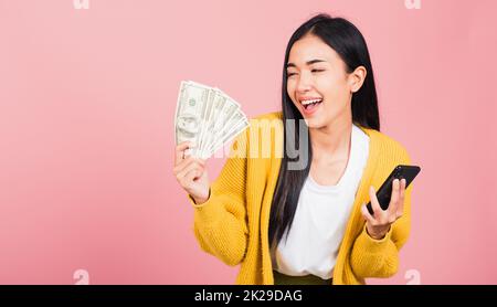 donna shopper sorridente in piedi eccitato tenere in mano il telefono cellulare intelligente online e banconote in dollari Foto Stock