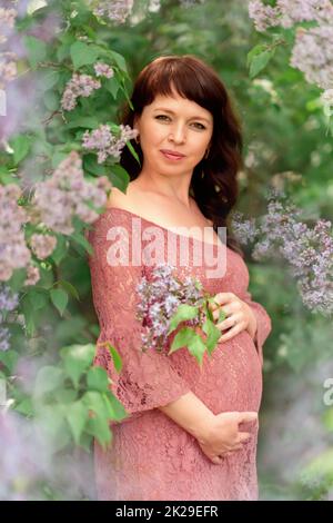 Una giovane donna incinta si erge nei cespugli lilla. Foto Stock