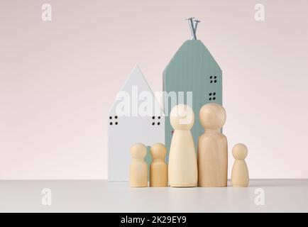 figure in legno di uomini e una casa in miniatura su sfondo beige. Il concetto di acquisto o vendita di immobili, mutui e assicurazione immobiliare Foto Stock