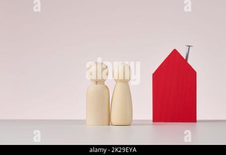 figure in legno di uomini e una casa in miniatura su sfondo beige. Il concetto di acquisto o vendita di immobili, mutui e assicurazione immobiliare Foto Stock