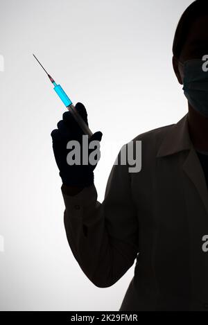 Silhouette di un medico con siringa riempita di liquido blu. Concetto di vaccinazione. Foto Stock