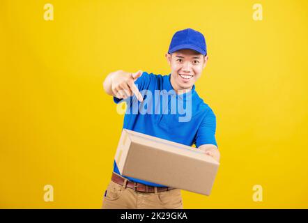 consegna uomo felice logistico in piedi lui sorriso indossare t-shirt blu e cappello uniforme tenendo la scatola pacchi puntando il dito verso la scatola Foto Stock