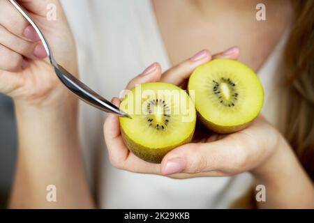 Kiwi frutta d'oro in mano. Ragazza che mangia kiwi maturo dorato con cucchiaio da dessert. Frutta per dieta sana e vitamina C concetto antiossidante. Foto Stock