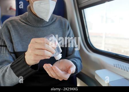 Viaggiare in sicurezza con i mezzi pubblici. Giovane uomo con maschera protettiva per il viso con dispenser di gel igienizzante per mani lavate. Il passeggero con maschera medica disinfetta le mani nel trasporto in treno. Foto Stock