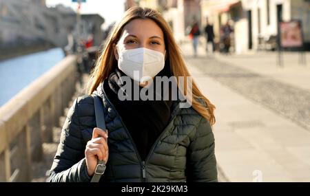 Bella giovane donna con maschera protettiva cammina lungo i canali dei Navigli a Milano Foto Stock