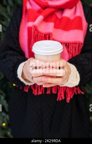 Una giovane ragazza in un cappotto e una sciarpa brillante tiene il caffè caldo nelle sue mani in una tazza usa e getta. Caffè da andare, escursioni. Foto Stock