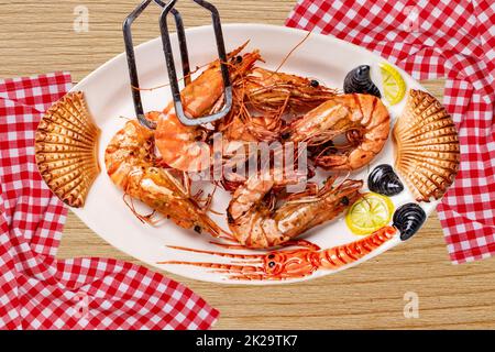 Barbecue di pesce sfondo. Primo piano di gamberi o gamberetti freschi grigliati su un piatto colorato di frutti di mare su un tavolo rustico con tela a plaid. Concetto di cibo sano. Pubblicità spaziale. Foto Stock