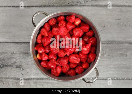 Vista del piano portapaziente, acciaio pentola piena di fragole con foglie rimosso. In casa confettura di fragole preparazione. Foto Stock