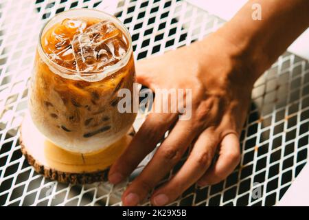 Tenere a mano il caffè latte ghiacciato in un bicchiere con la crema sul fondo. Freddo fondo bevanda estiva Foto Stock