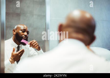 Un ritratto di un uomo nero calvo adulto bello e bearded imprenditore in una camicia bianca con una cravatta che pettina la barba con un pettine rosa in una res pubblica Foto Stock