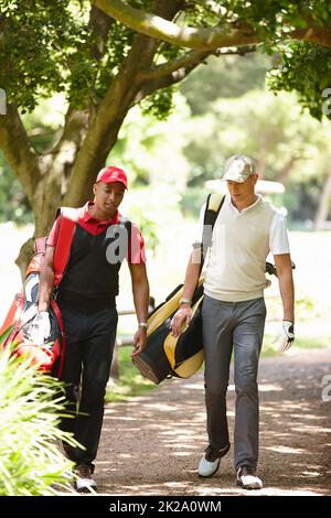 Tornando a casa dopo una giornata di golf, due uomini camminano lungo un sentiero ombreggiato su un campo da golf. Foto Stock