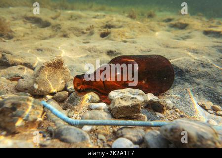 Piccolo marrone bottiglia di birra e di plastica blu paglia di sabbia sul fondo del mare. Foto subacquee, oceano littering concetto. Foto Stock