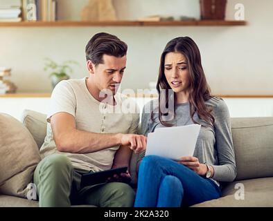 Le nostre spese cominciano a farsi di mano. Scatto di una giovane coppia che passa attraverso il loro lavoro di ufficio insieme a casa e guardando preoccupato. Foto Stock