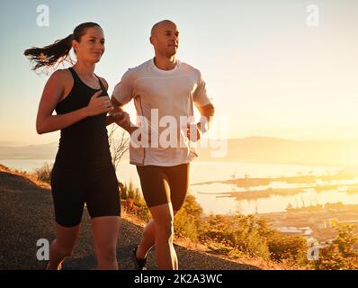 La corsa fa parte della loro routine quotidiana. Scatto di una giovane coppia che corre insieme lungo una strada. Foto Stock