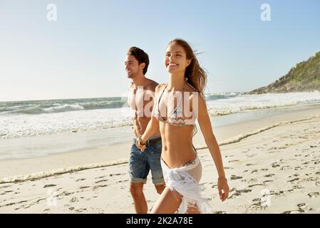 Buon giorno in spiaggia. Scatto di una giovane coppia romantica che cammina a mano sulla spiaggia. Foto Stock