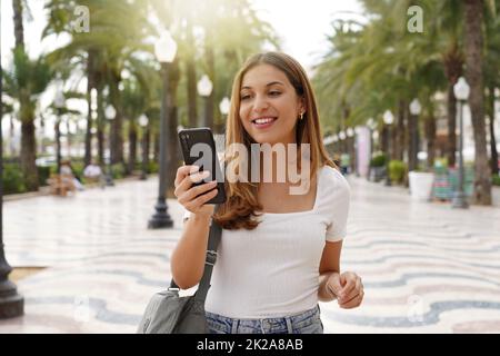 Ragazza di viaggio che cerca un hotel sul cellulare. Sorridente turista femmina prenotare una camera per la notte con smartphone. Concetto di viaggi last minute. Foto Stock