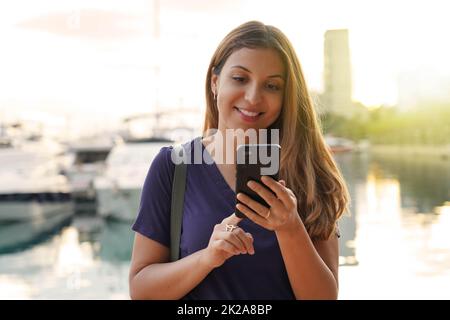 Ragazza turistica che scorre sullo schermo a sfioramento dello smartphone in cerca di hotel. Viaggiatore donna che digita sul telefono cellulare e prenota una camera per la notte. Concetto di viaggio last minute. Foto Stock