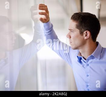 Che cosa tiene il mio futuro? Un giovane uomo d'affari in piedi contro un muro di vetro che guarda preoccupato. Foto Stock