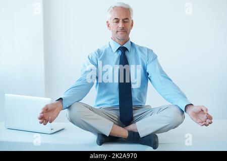 Trovare il suo centro. Scatto a tutta lunghezza di un uomo d'affari maturo seduto a gambe incrociate e meditating. Foto Stock