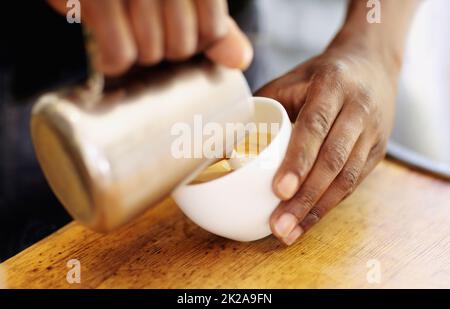 Per tagliare il cappuccino. Shot di un barista che versa la schiuma di latte in un cappuccino. Foto Stock