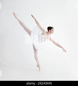 L'equilibrio è fondamentale. Elegante ballerina giovane in pointe su sfondo bianco in posizione penche. Foto Stock