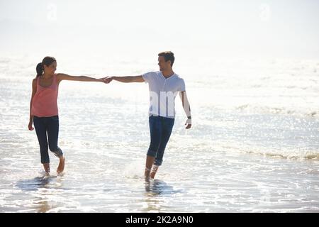 Tu sei il mio su 6 miliardi. Scatto di una giovane coppia che tiene le mani mentre cammina vicino alla spiaggia. Foto Stock