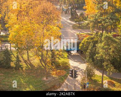 I lavoratori con spazzatrice a vuoto su un trattore con rimorchio raccolgono le foglie cadute in un bellissimo parco cittadino colorato giallo, arancione e verde autunno. Foto Stock