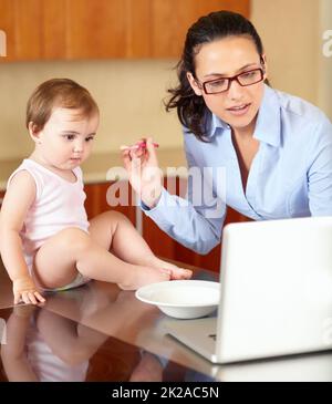 Una mano supplementare sarebbe utile. Scatto di una mamma che allatta il suo bambino mentre cerca di lavorare sul suo laptop. Foto Stock