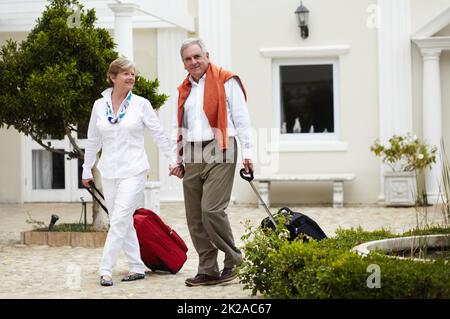 Anticipare una meritata vacanza. Ritratto di una coppia anziana che arriva al loro hotel con le loro valigie in stoppa. Foto Stock