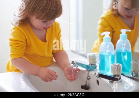 Guarda, il suo correre attraverso le mie dita. Una bambina adorabile che lava le mani in bagno. Foto Stock