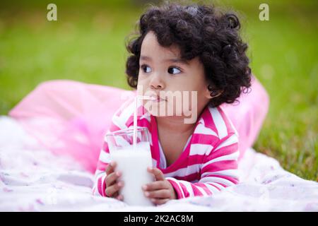 Mmmmm. Adorabile bambina che beve latte attraverso una paglia mentre si trova sull'erba. Foto Stock