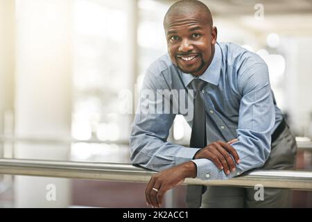 Fiducia aziendale. Ritratto corto di un uomo d'affari che si appoggia contro una ringhiera nel corridoio dell'ufficio. Foto Stock