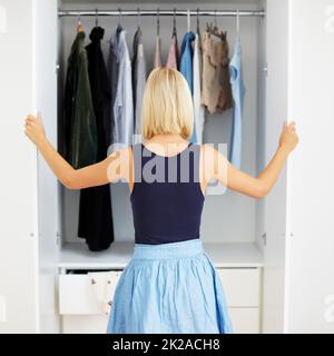 Armadio a muro pieno di scelte. Vista posteriore di una giovane donna bionda che sceglie un vestito nel suo armadio. Foto Stock