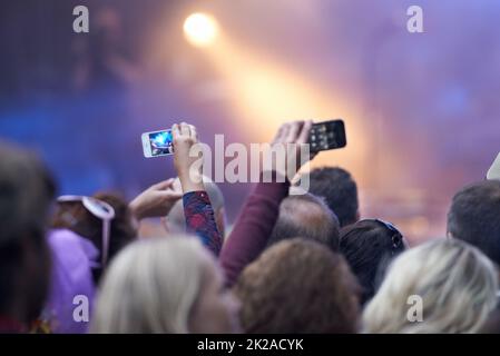 Cattura l'attimo. Dietro l'inquadratura di una folla in un festival musicale con due persone che tengono in mano i loro telefoni cellulari con fotocamera. Foto Stock