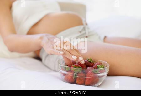 Ottenere quelle calorie supplementari sotto forma di uno spuntino sano. Immagine ritagliata di una donna incinta con una ciotola di fragole. Foto Stock