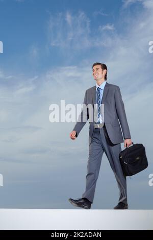 Passeggiando verso il successo. Un giovane uomo d'affari che porta la sua valigetta contro un cielo blu. Foto Stock