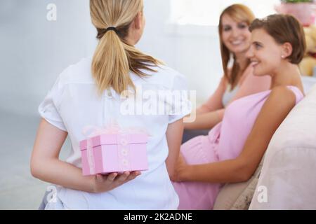 Prolungamento dell'attesa. Una giovane donna che nasconde un regalo dietro la schiena ai suoi amici babyshower. Foto Stock