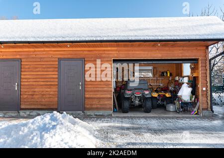 Vista sulla facciata porta aperta ATV casa garage con quad fuoristrada veicolo parcheggiato sole neve fredda giornata invernale. ATV avventura sport estremo. Casa organizzata Foto Stock