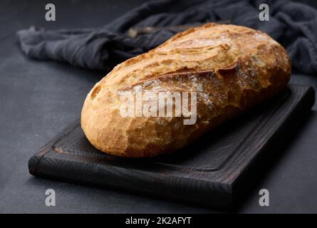 pane ovale intero cotto a forno a base di farina di grano bianco su un tavolo nero Foto Stock