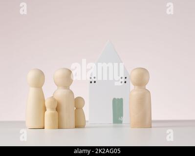 figure in legno di uomini e una casa in miniatura su sfondo beige. Il concetto di acquisto o vendita di immobili, mutui e assicurazione immobiliare Foto Stock