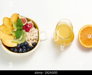 un piatto con farina d'avena e frutta, mezzo succo d'arancia maturo e spremuto di fresco in un decanter trasparente in vetro su un tavolo bianco. Colazione sana Foto Stock