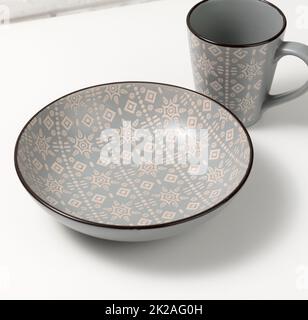 svuotare il piatto di zuppa in ceramica grigia e svuotare la tazza sul tavolo bianco, utensili Foto Stock